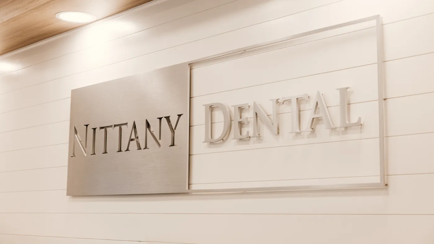 The brushed-steel Nittany Dental sign on the lobby wall